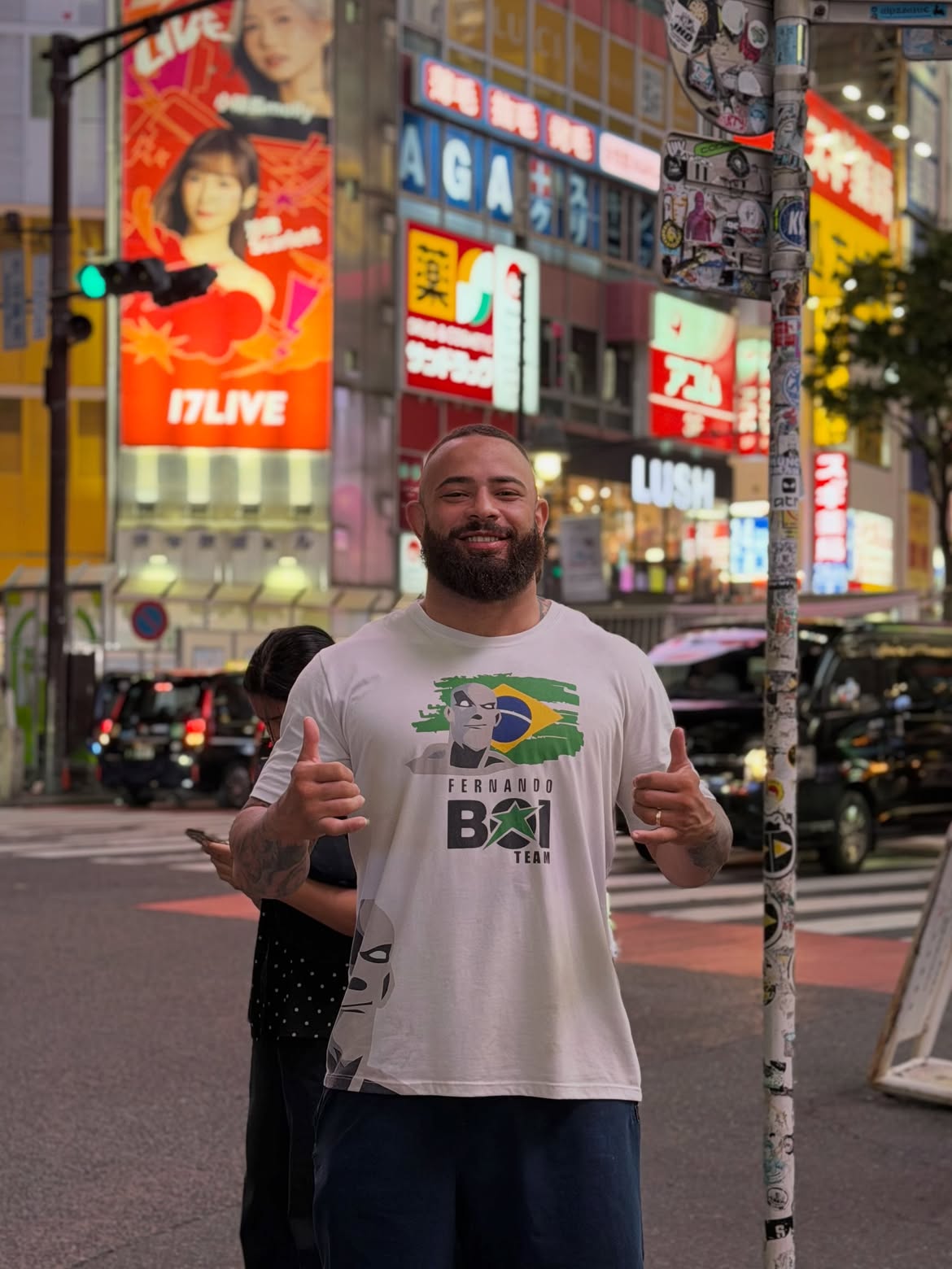 Uriel Meneses sorrindo em uma rua de Tóquio, com camiseta estampada com a bandeira do Brasil